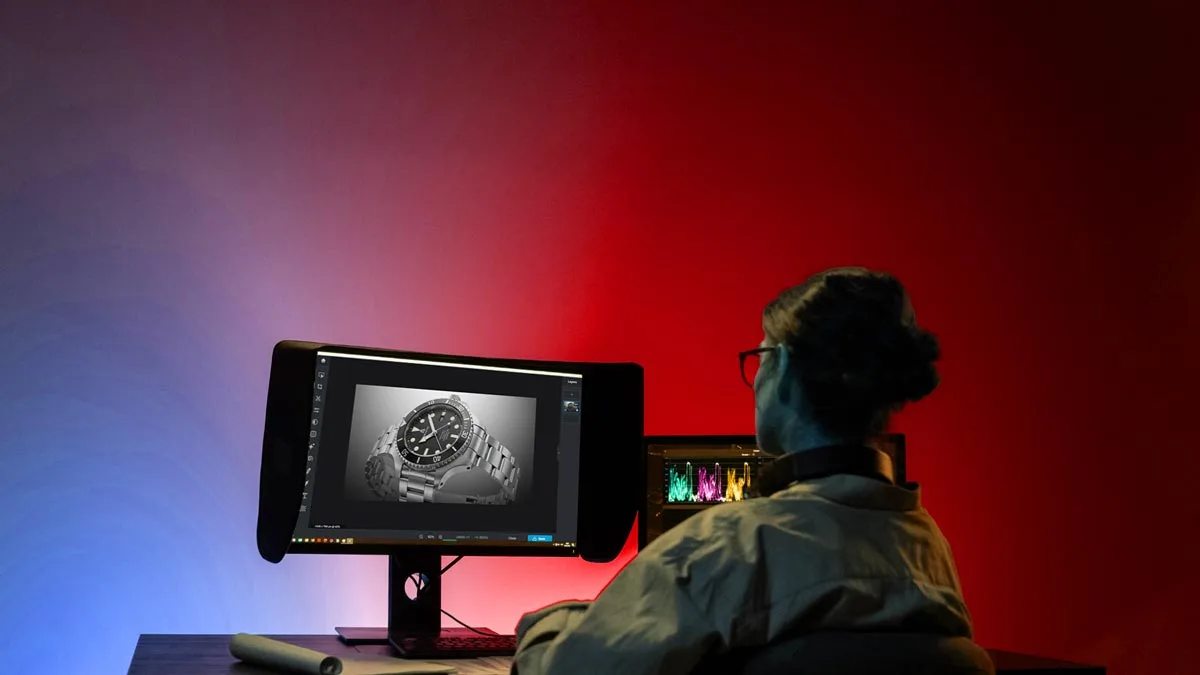 Photo editor working on a desktop monitor with an image of a watch, surrounded by a colorful gradient lighting effect in a dark room.